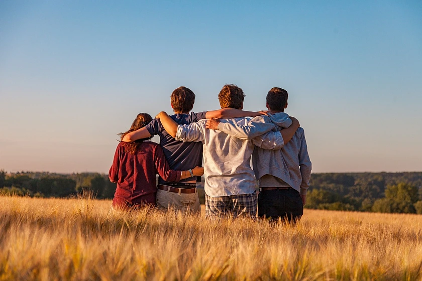 Vier Jugendliche stehen Arm in Arm auf einem Kornfeld mit dem Rücken zum Fotografen